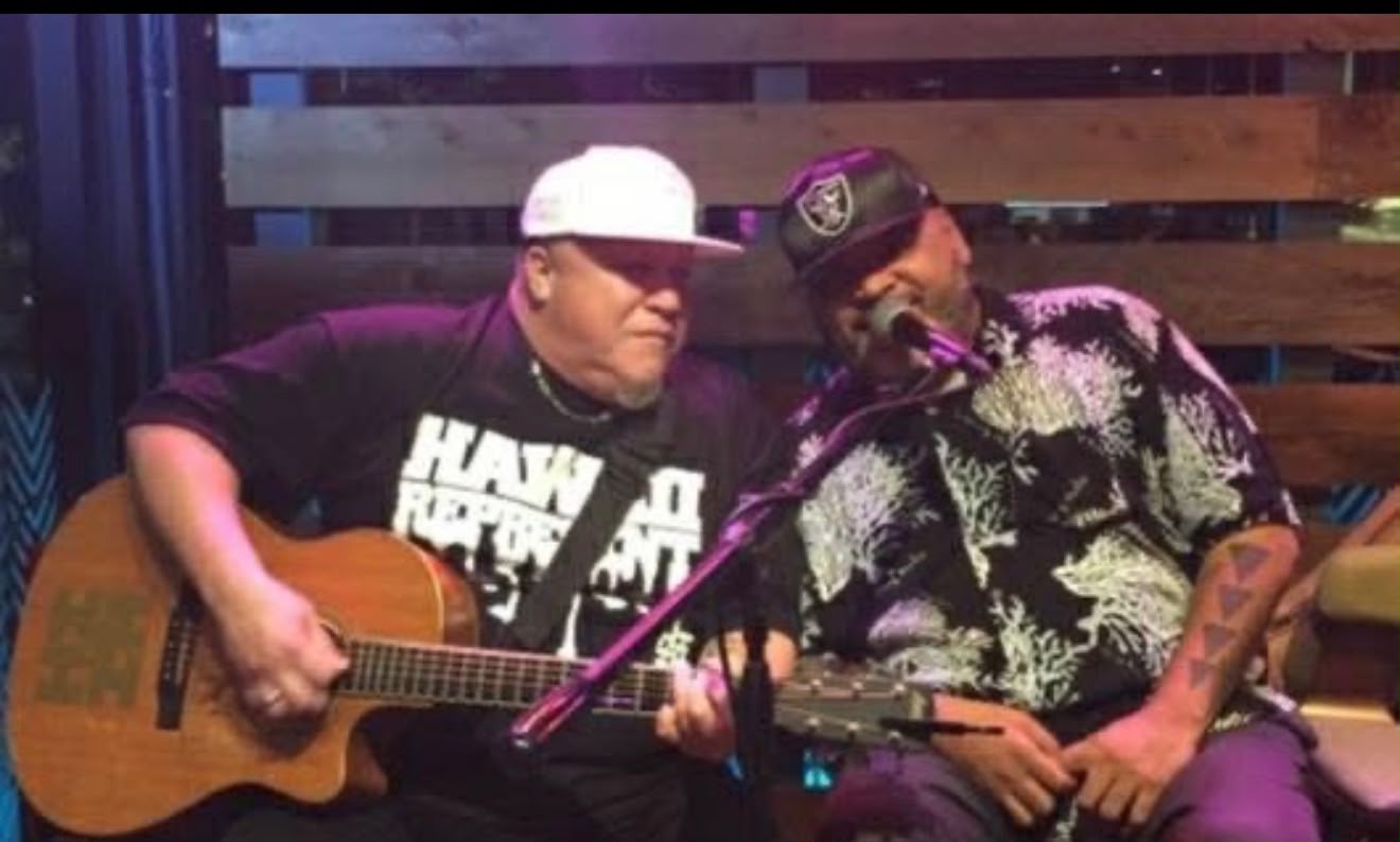 Jeff Rasmussen playing acoustic guitar beside George “FIJI” Veikoso at a microphone