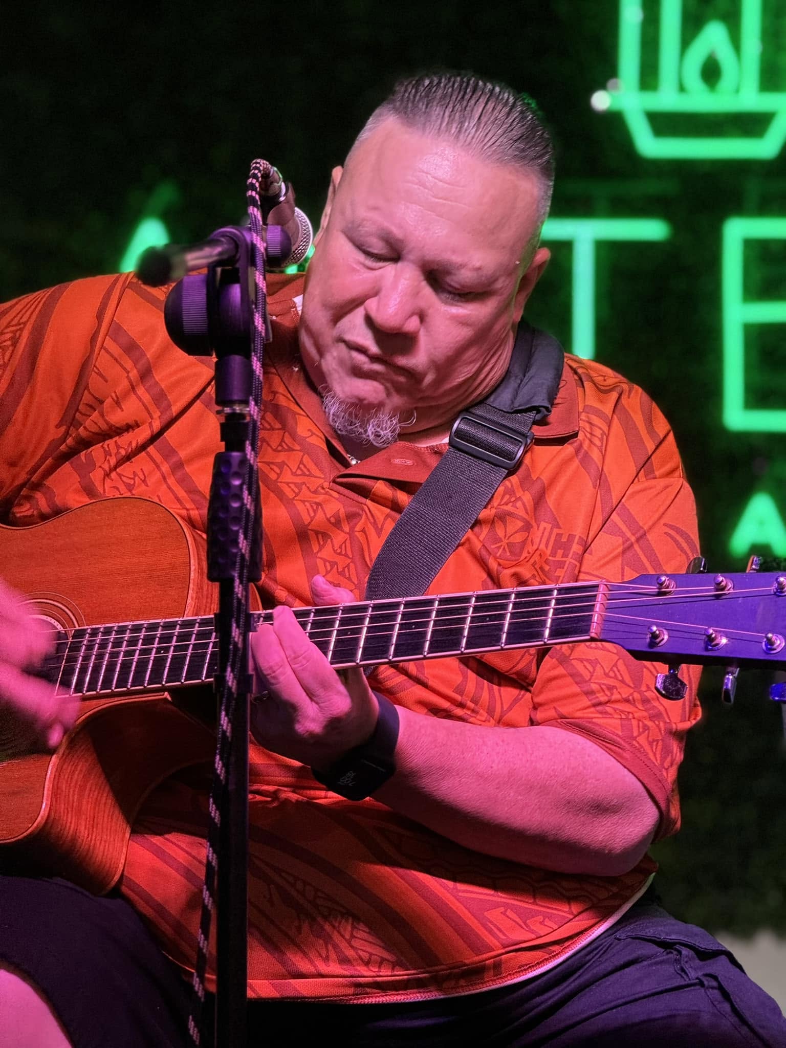 Jeff Rasmussen performing on guitar in an orange aloha shirt